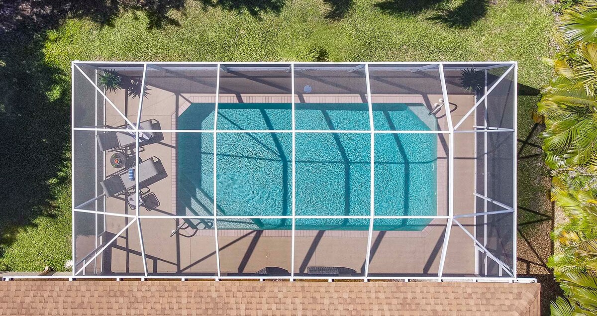 Beheizter Pool mit Sonnenliegen und Blick in den großen, privaten Garten mit Grill.