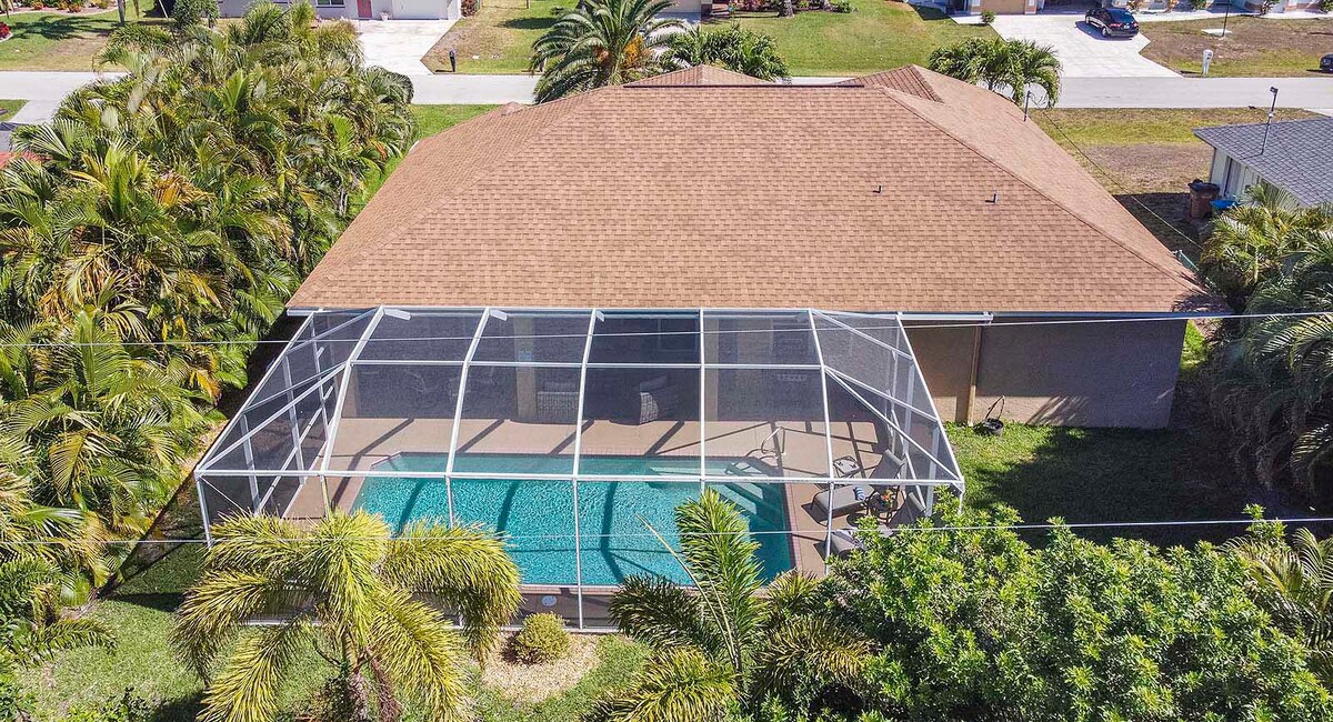Beheizter Pool mit Sonnenliegen und Blick in den großen, privaten Garten mit Grill.
