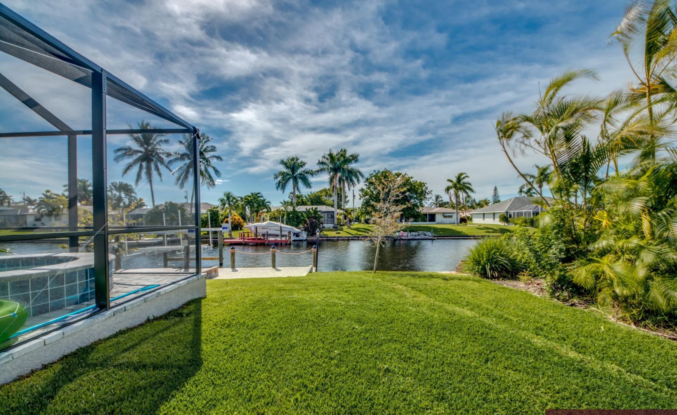 Sonnige Poolterrasse am Kanal mit Bootsdock und Blick aufs Wasser.