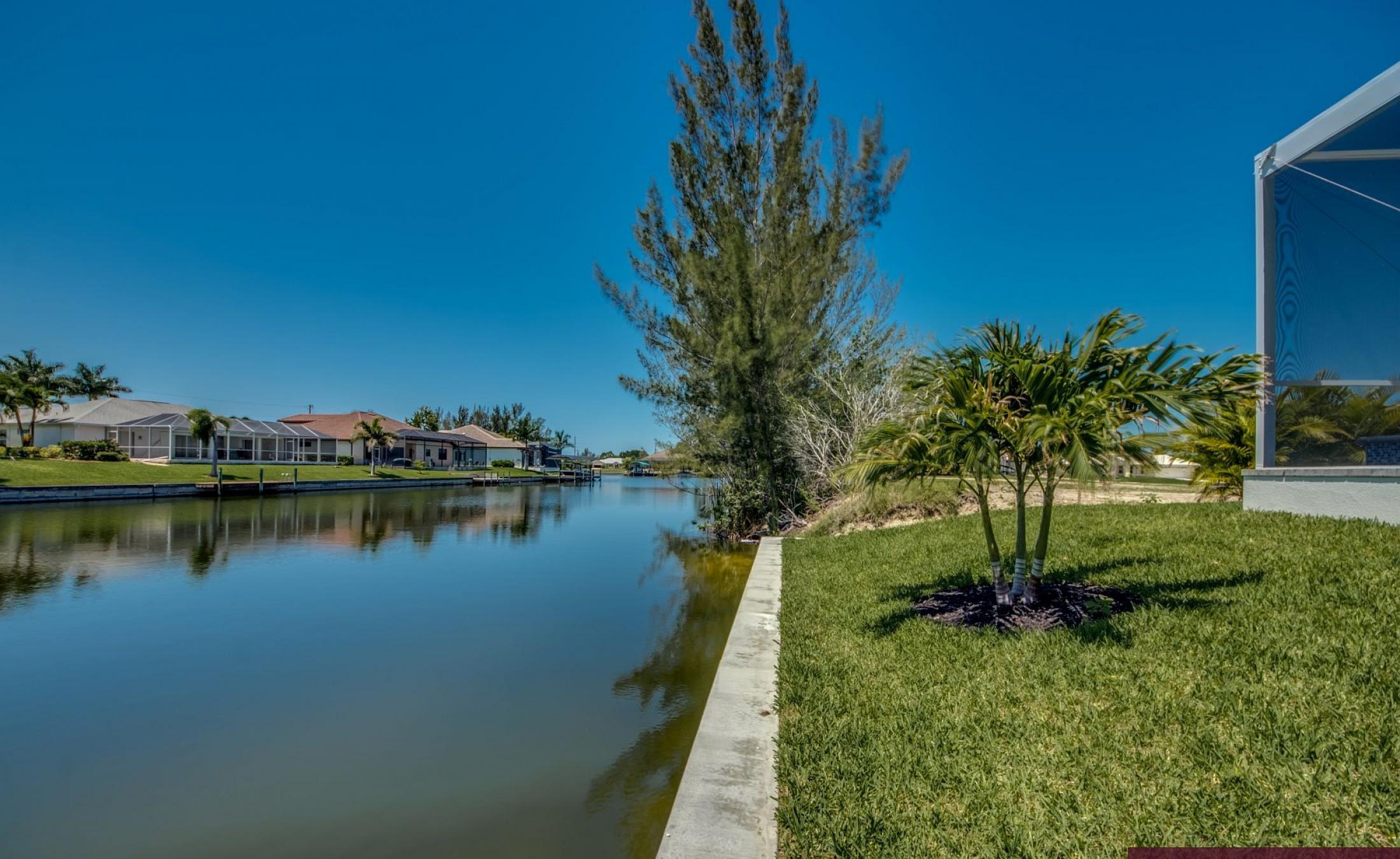 Sonniger Poolbereich am Kanal mit privatem Bootsdock und Blick aufs Wasser.