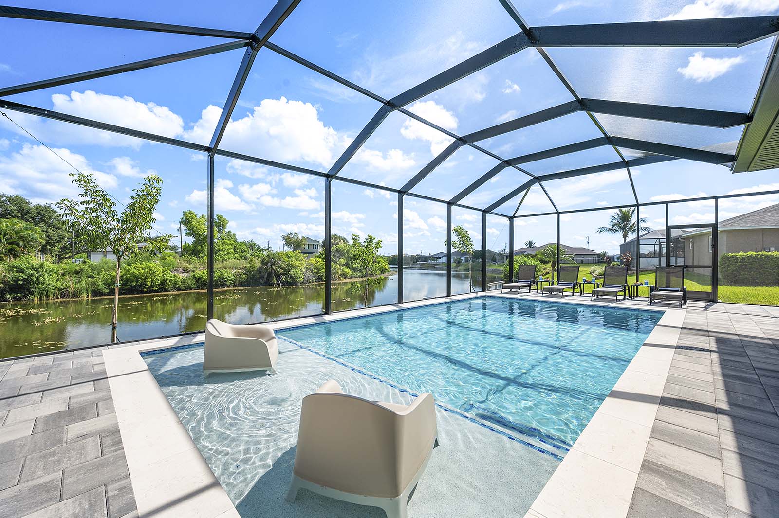 Großer Poolbereich mit Sonnenliegen, Outdoor-Küche und TV unter der überdachten Lanai.